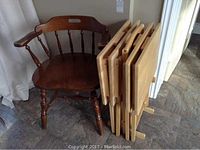 Wooden captain's chair next to a folded set of 4 TV tables stored on a wooden stand.