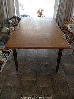 Rectangular wooden harvest table with pine top and painted legs, showing overall wear.