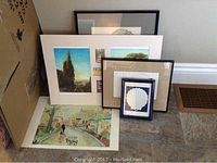 Framed and matted artworks displayed together, showing different sizes and subjects including landscapes and shell print.