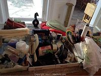 Photo showing an assortment of kitchen and household items including placemats, napkins, plastic containers, and various kitchen gadgets packed in boxes.