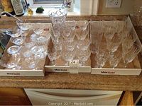 Collection of cross and olive crystal stemware glasses arranged in boxes on a countertop showing different sizes and types of glasses, including small bowls and goblets.