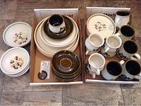 Overview of the entire stoneware dinnerware set showing the various plates, bowls, cups, and saucers in two cardboard boxes on the floor.