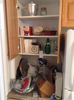 Photo of cupboard with various kitchen items including ironstone jug, metal charger plates, kitchen scale, cookbooks, and other kitchenware.