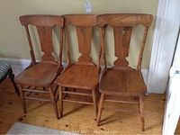 Three wooden kitchen chairs side by side against a wall, showing the overall shape and design.