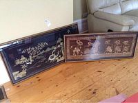 Two framed native-themed textiles placed on the floor leaning against a wall, showing full front view