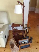 Full view of wooden floor lamp with integrated side tables and magazine rack, wicker basket, fireplace utensils, and cast iron pieces on wooden floor