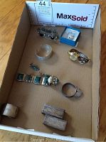 Photo of all items in a cardboard box from above showing bracelets, ring, watch, napkin rings, and small jewelry pieces
