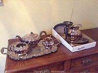 Full lot arranged on dresser including silverplate tea service with teapot, creamer, sugar bowl on tray, additional trays, water jug, and vase, seen from front