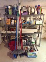 Wide shot of metal utility shelving filled with various cleaning supplies, red bucket, and cleaning tools including brooms and mop leaning against it.