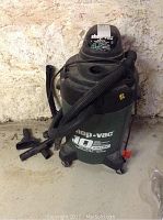 Front view of green and black Shop-Vac unit with hose and accessories attached, showing overall condition and design.