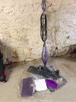 Photo of upright purple Shark floor steamer with coiled cord and accessories on the floor.