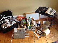 Photo shows a collection of household items including a Weight Watchers scale, cleaning sprays, shoe rack, adjustable TV table with a telephone on top, whiteboard, umbrella stand, and various small items arranged on a wooden floor against a beige wall.