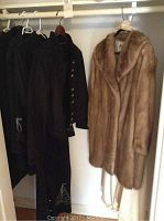 Closet view showing the light brown mink coat next to three black coats hanging on a rod.