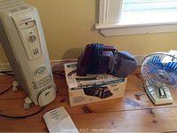 Noma oil filled radiator positioned on wooden floor beside Douglas power brush and fan, showing all items in the lot