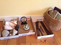 Photo showing two leather straps, two railway spikes placed in a cardboard tray, basket filled with books, seashells, and a small white ceramic flower decoration.