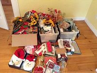 Overview of mixed Christmas decorations in plastic bins and boxes showing fabric Santa heads, floral arrangements, and assorted napkins and decor pieces.