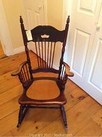 Front view of early wooden rocking chair showing carved top backrest, armrests, and contoured seat with wear.