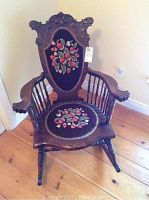Front view of carved wooden rocking chair with floral needlepoint seat and back
