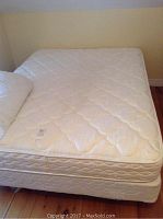 View of queen mattress on box spring with a mattress pad folded on one corner, showing quilted white design.