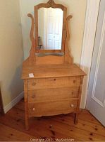 Frontal view of wooden dresser with three drawers and swing mirror against wall.
