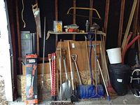 Various garden tools including rakes, shovels, pitchfork, saws, a garbage can, and Black & Decker trimmer/edger boxed