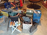 View of assorted bags of mulch, soil, small garden tools, crates, and chairs in a garage setting.