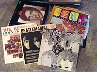 Box of assorted vinyl record albums including Beatles, Elvis Presley, classical and others placed on the floor, showing wear and aging.