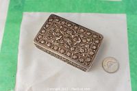 Closed rectangular silver snuff box showing floral relief carving on lid with coin for scale