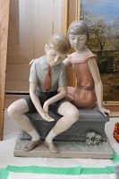 Front-side angle of Lladro boy and girl statue showing detailed faces and clothing on a stone bench