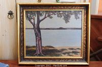 Framed oil painting showing a lake scene with foreground trees and calm water landscape.