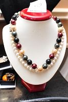 Full view of the two necklaces displayed on a bust. One necklace is composed of white freshwater pearls, the other has large multicolor beads including black, maroon, gold, and dark green.