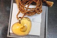 Heart-shaped yellow Lalique pendant with smaller heart cutout on brown twisted cord, presented in jewelry box