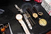 Seven watches arranged on dark table surface, showing various styles including ladies GUESS watch, DKNY, Gucci, Timex, Seiko, Swarovski, and Ingraham pocket watch.
