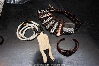 Full view of copper bracelet with turquoise stone, carved bone pendant, and dark brown and white bead necklace on a black surface.