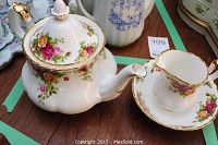 Photo showing the tea pot with floral pattern and gold accents along with creamer and saucer on wooden table