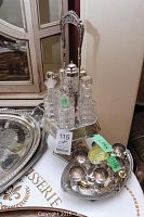 Six-piece glass cruet set in silver-tone metal stand with handle, placed next to metal egg cups on tray.