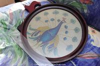 Photo showing the beaded glass peacock art laying on fabric with visible details of the peacock design and wooden frame handle.