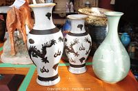 Three vases: two white crackle glaze dragon motif vases and one celadon green vase on wooden table
