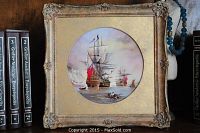 Full view of square gold gilt frame with round porcelain painting of ships on water