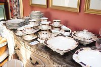 Full view of the Myott Son & Co Derby china set arranged on a sideboard against a red wall, showing stacks of plates, cups, saucers, and serving dishes.