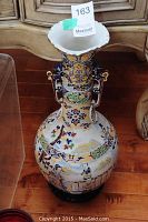 Tall Asian ceramic vase with flared scalloped white rim and colorful raised relief figurative and floral designs on body and neck, with decorative handles