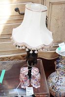 Carved wood lamp with fabric lampshade that has tassels, shown next to ceramic cats on glass table.