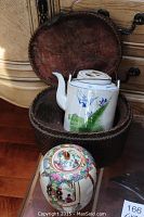 Woven basket holding white ceramic tea pot and colorful lidded vase