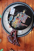 Large round Asian charger plate with colorful hand-painted design seated on wooden display stand, placed atop white plate.