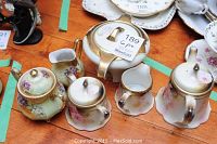 Photo showing six porcelain tea set pieces with floral patterns and gold accents, including teapot, creamer, sugar pot, lidded jar, and cream and sugar containers.