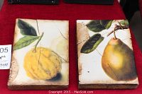 Front view of two rectangular decorative tiles on red cloth, one depicting a lemon and one depicting a pear