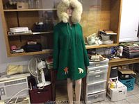 Full front view of green ladies coat with fur-lined hood on mannequin, displaying the native hunting scene embroidery with polar bears and igloos on bottom hem and sleeves.