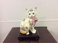 Front view of hand painted Franklin Mint porcelain cat figurine with floral patterns and pink bow, on dark wooden base