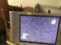 Sharp Aquos 19-inch flat-screen TV showing test screen with static/no signal, featuring integrated side speakers, mounted for display.