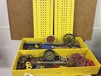 Original yellow metal box with assortments of Meccano toy building parts including metal strips and wheels